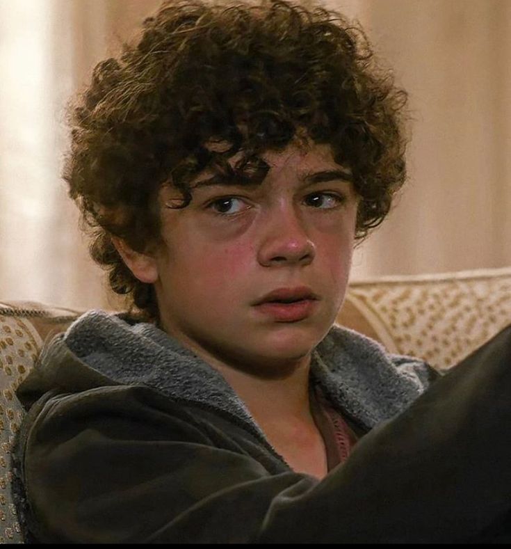 a young boy sitting on top of a couch holding a remote control in his hand