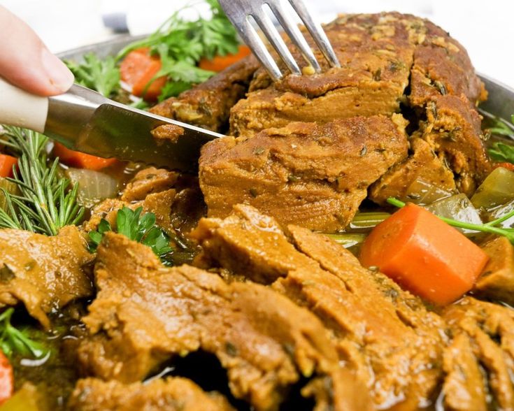 a person cutting meat with carrots and parsley on the side in a pan