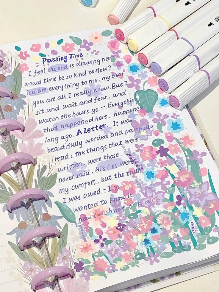 an open book with flowers and writing on it next to crayon markers, pens and pencils