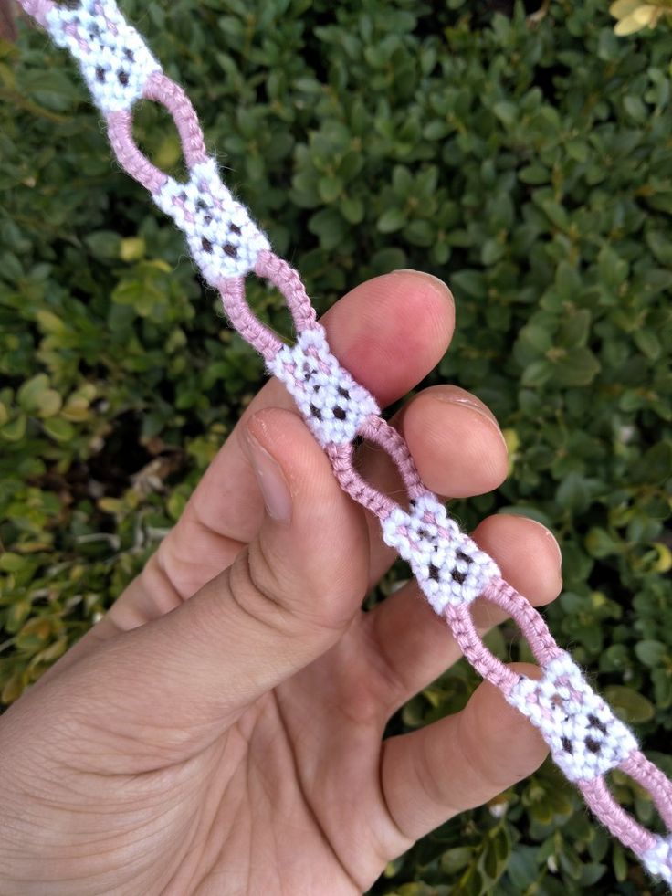 someone is holding up a crocheted chain in front of some bushes and shrubbery