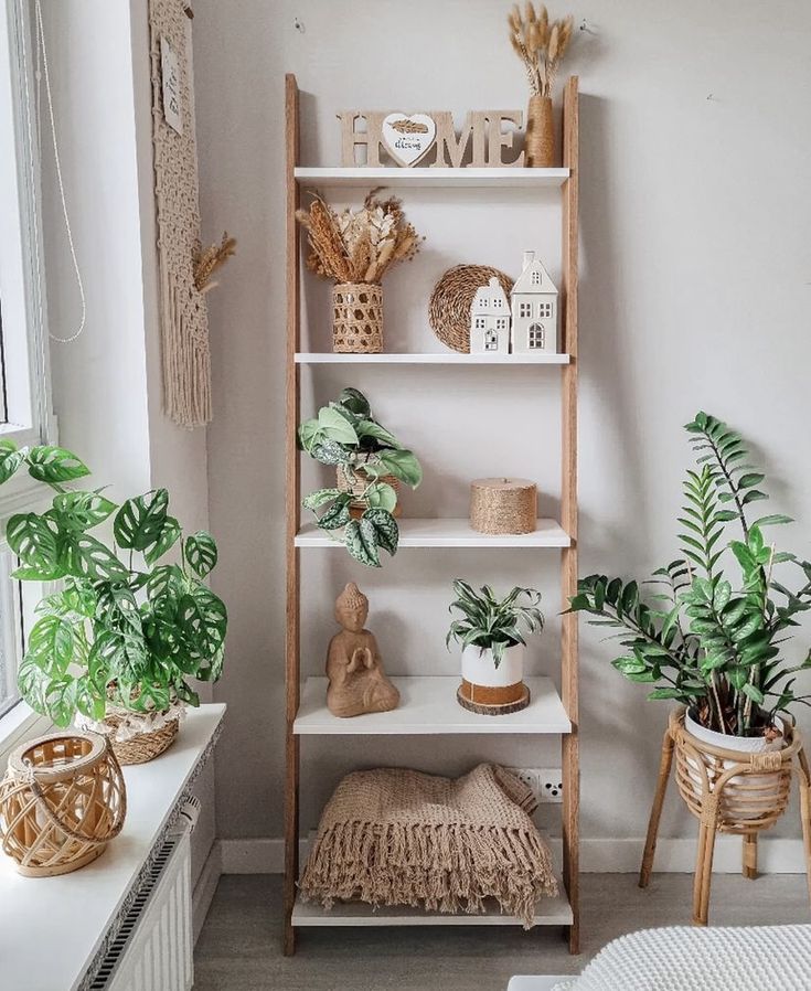 a white shelf with plants and other items on it in a room next to a window