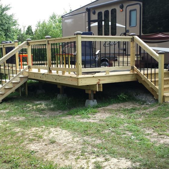 a deck built into the side of a trailer with stairs leading up to it and a motor home in the background