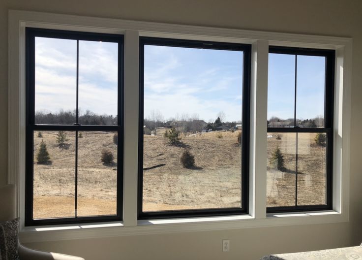 an empty room with three large windows overlooking a field and trees in the foreground