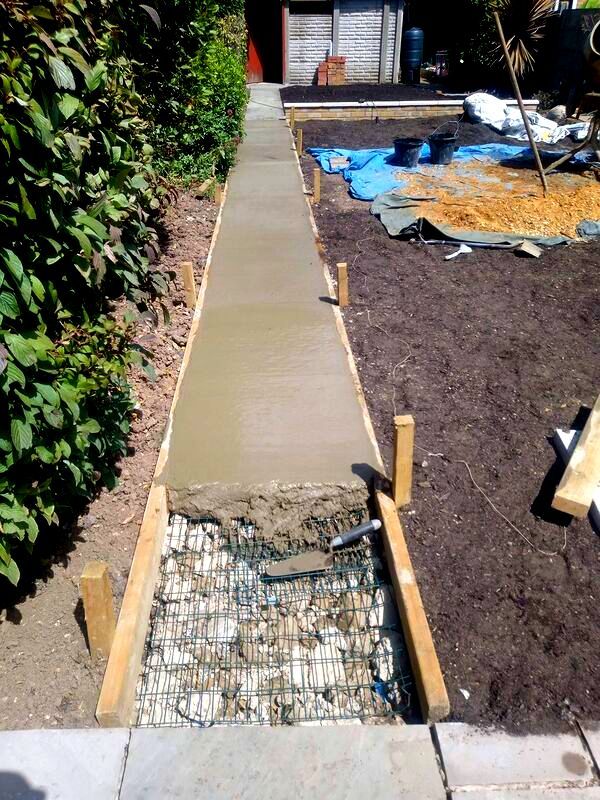 a concrete walkway is being built in the yard with plants and dirt around it,