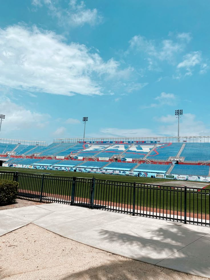 an empty stadium with blue seats on the side and green grass in the foreground