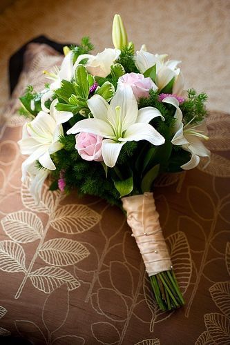 a bridal bouquet with white lilies and pink roses sits on a bed sheet