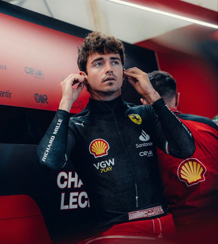 a man sitting in front of a red wall holding his hand to his ear while wearing a black suit