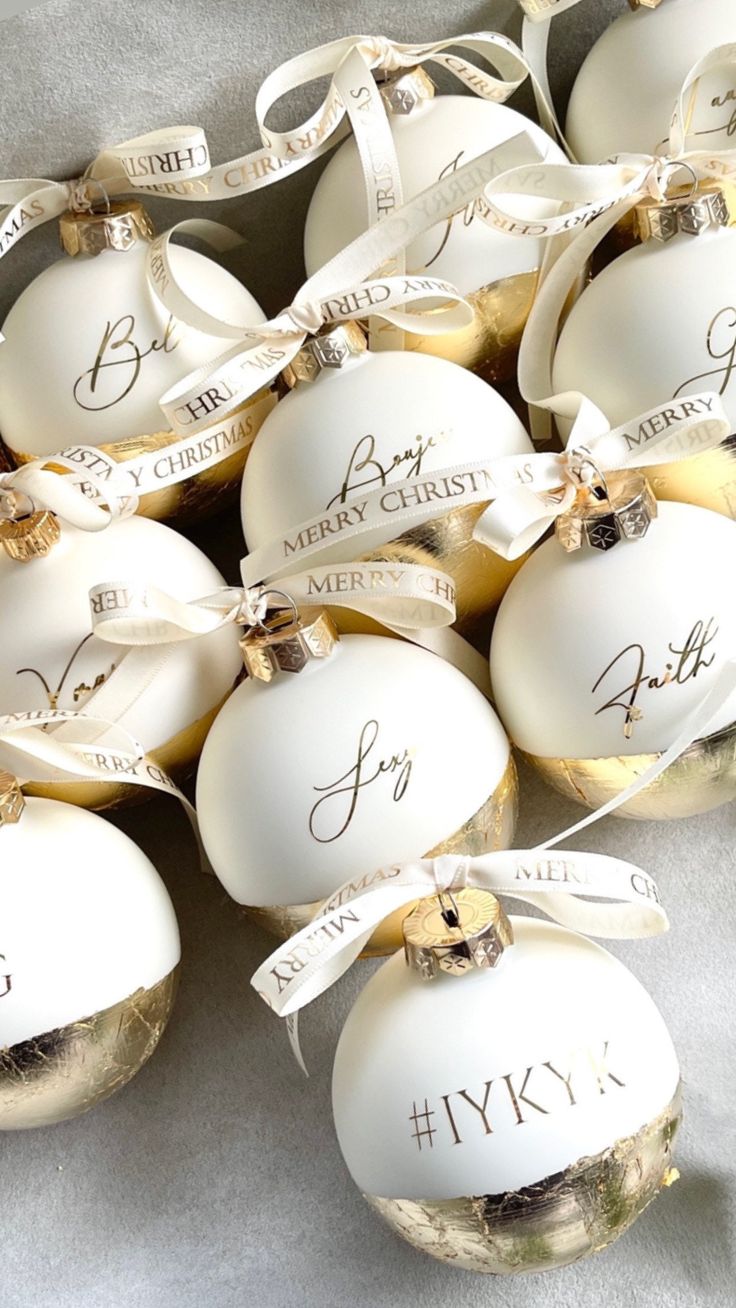 twelve white christmas baubles with names and ribbons on them, all decorated in gold