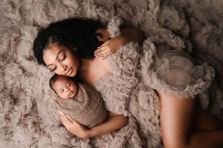 a woman holding a baby in her arms while laying on top of a fluffy blanket