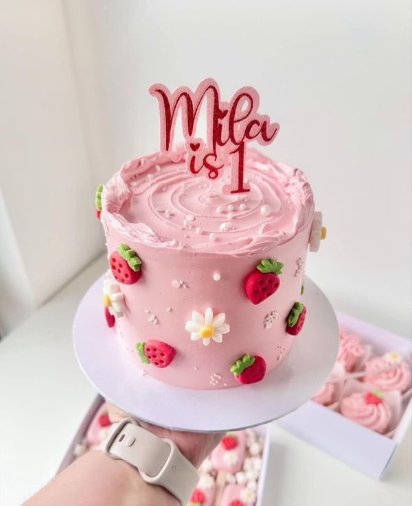 a pink cake with strawberries and flowers on it is being held up by someone's hand