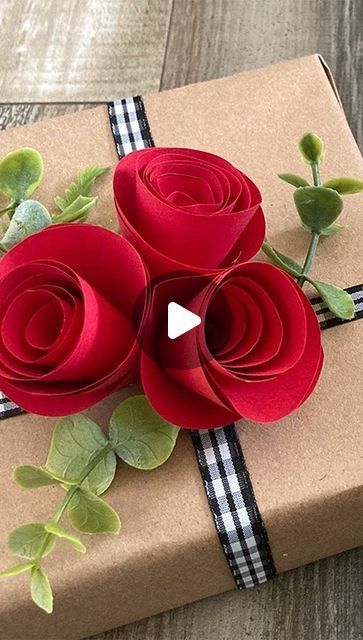 a gift wrapped in brown paper with three red roses on the top and green leaves