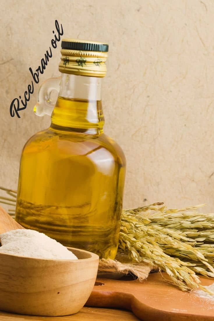 a bottle of rice bran oil next to a wooden spoon on a cutting board with ears of wheat