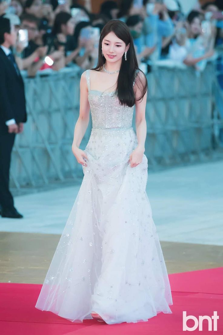 a woman in a white dress standing on a red carpet