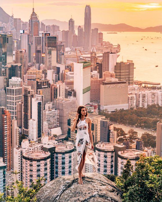 a woman standing on top of a large rock in front of a cityscape