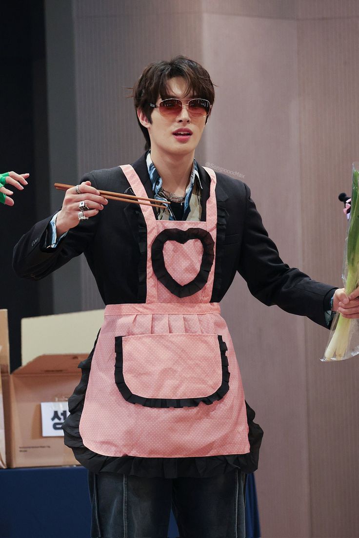 a man in an apron holding vegetables and chopsticks