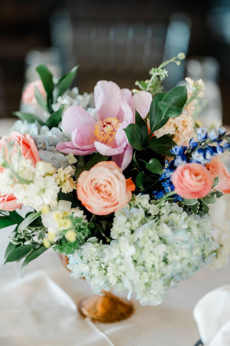 Image of the wedding reception space at the Cape Club of Sharon, a wedding venue in Massachusetts. The photo is zoomed in on a pastel Wedding Flower Centerpiece featuring pink peonies, ink roses and blue hydrangeas. 

Photo by Ali B Photography Pastel Wedding Flowers Centerpieces, Pastel Wedding Ceremony, Roses And Peonies, Pastel Wedding Flowers, Flower Centerpiece, Blue Hydrangeas, Peony Wedding, June 1st, Pastel Palette