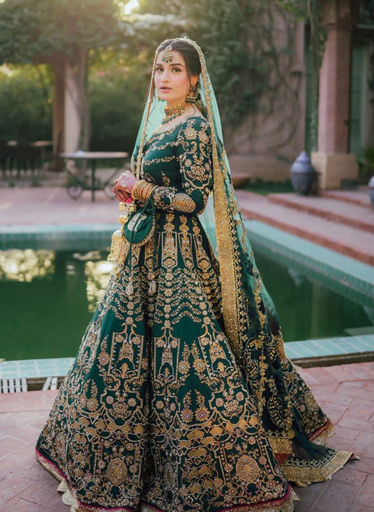 a woman in a green and gold bridal gown standing next to a swimming pool