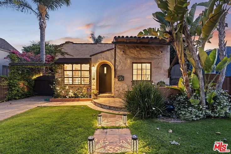 a house that is in the grass with palm trees and bushes around it, at dusk