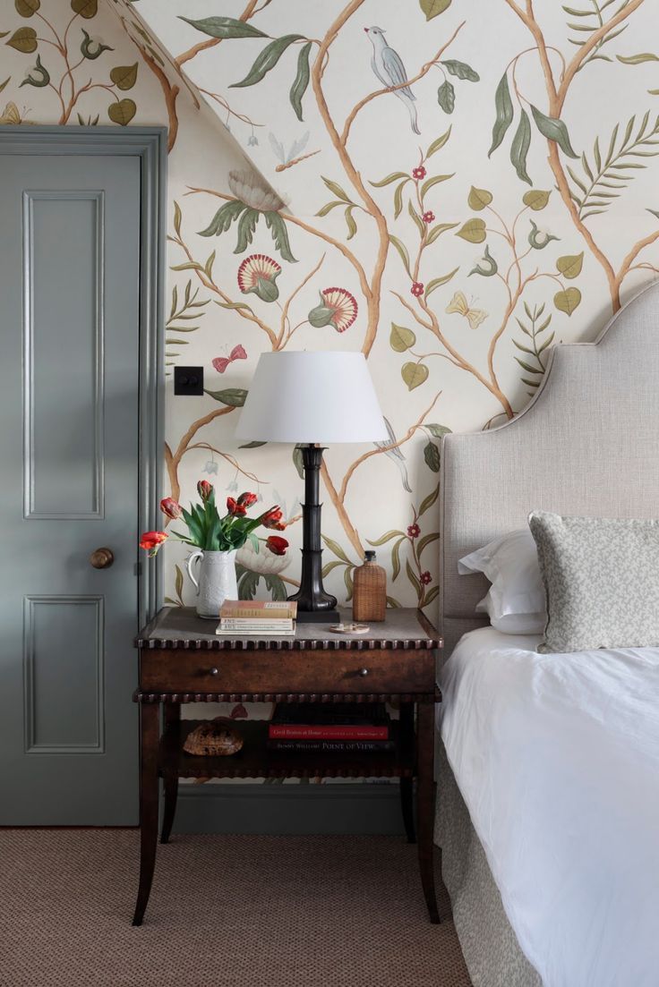 a bedroom with a bed, nightstand and wallpaper on the walls is decorated with flowers