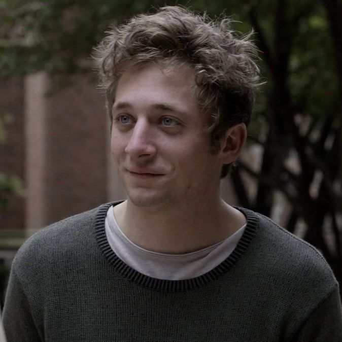 a young man with curly hair is looking at the camera while standing in front of a tree