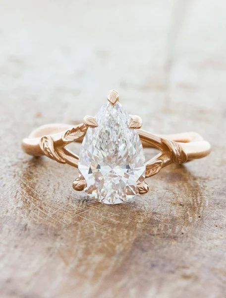 a pear shaped diamond ring sitting on top of a piece of wood with vines around it