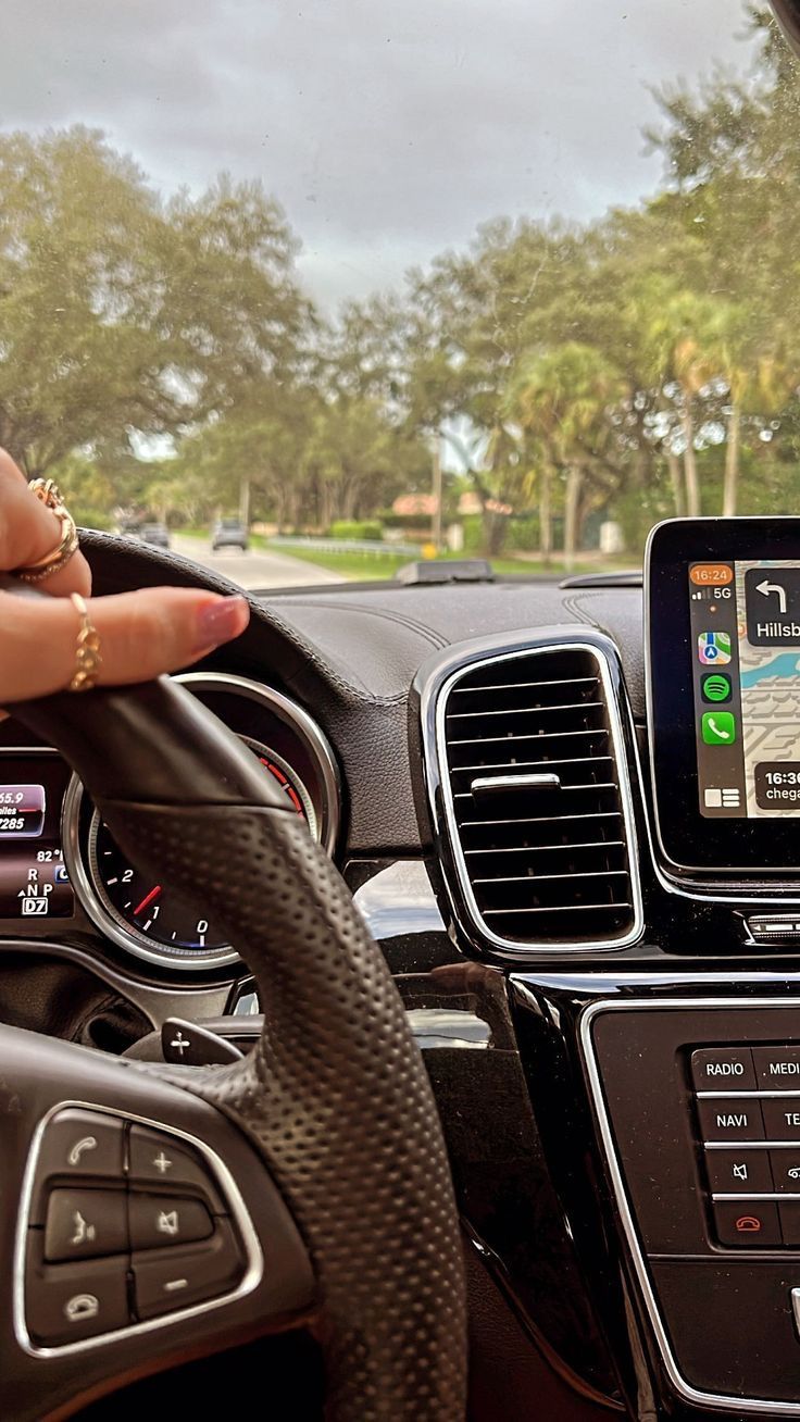 a person is holding their hand on the steering wheel of a car while looking at an electronic device