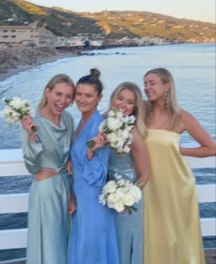 four women in long dresses posing for a photo on the deck of a boat with flowers