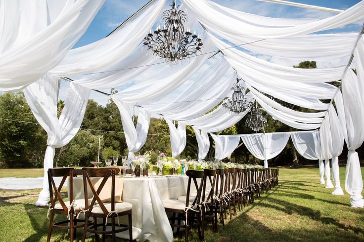 an outdoor wedding setup with white drapes and chandelier