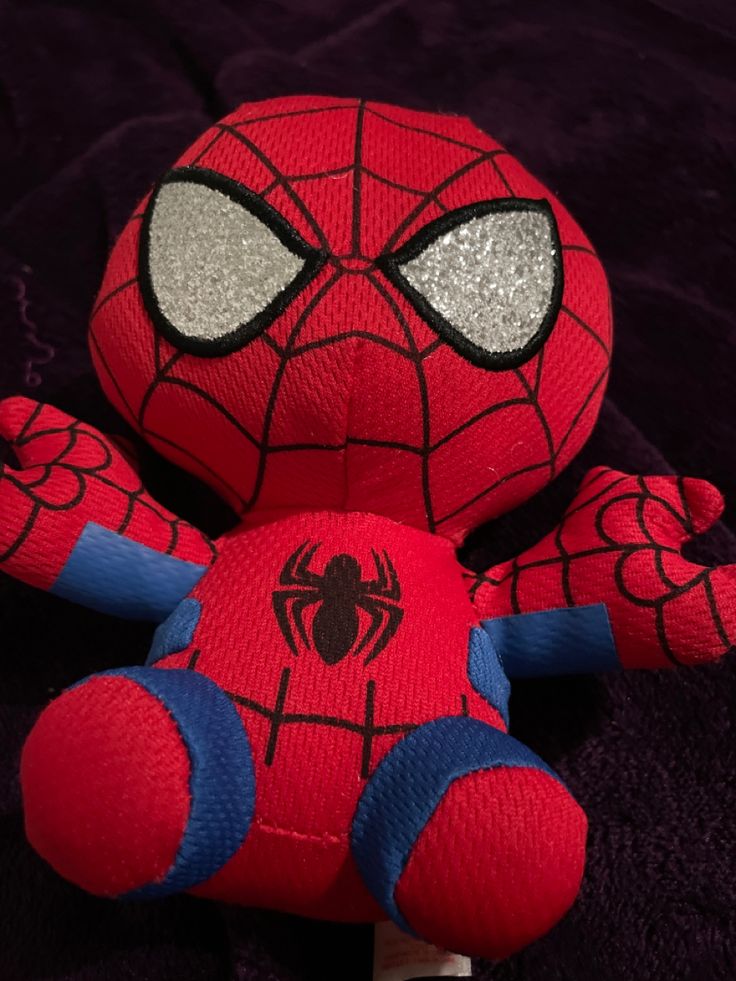 a spiderman stuffed animal sitting on top of a purple blanket