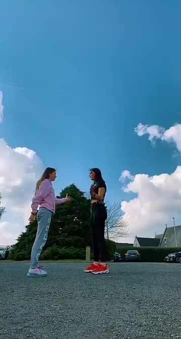 two women standing in the middle of a parking lot with a kite flying above them