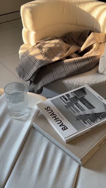 an open book sitting on top of a bed next to a glass cup and blanket