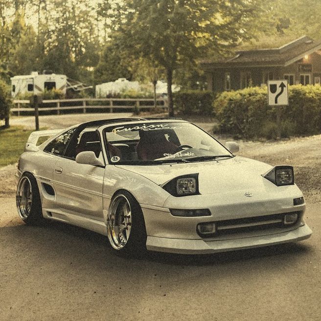 a silver sports car parked in front of a house on the side of a road