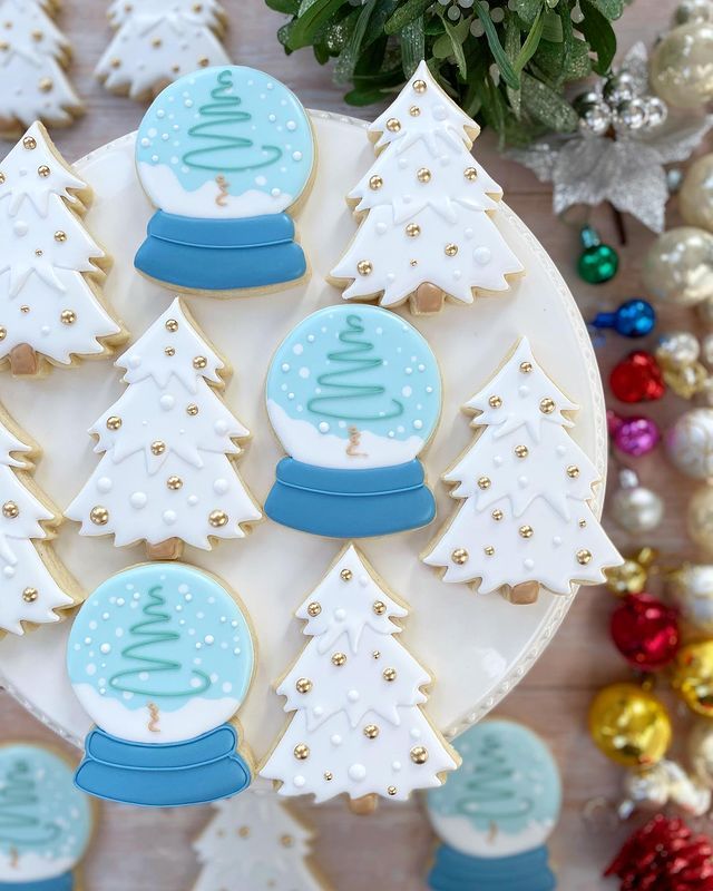 decorated cookies on a plate with christmas trees and snow globes in the middle, surrounded by other holiday decorations