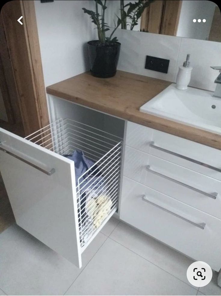 a white sink sitting under a bathroom mirror next to a wooden counter with a plant in it