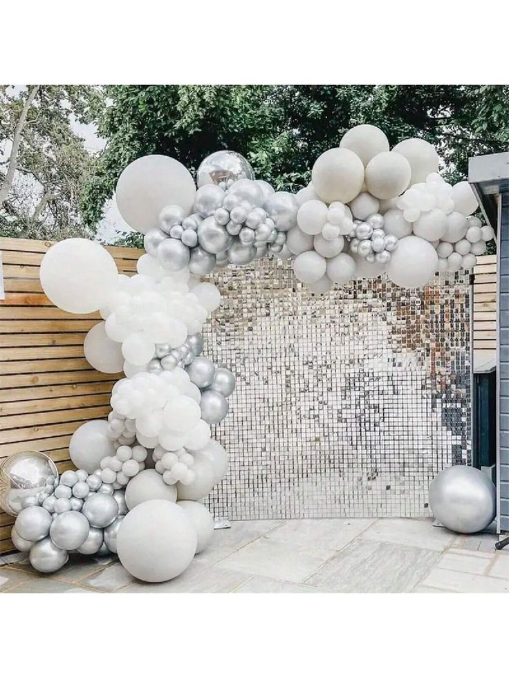 white and silver balloons are hanging from the side of a gate