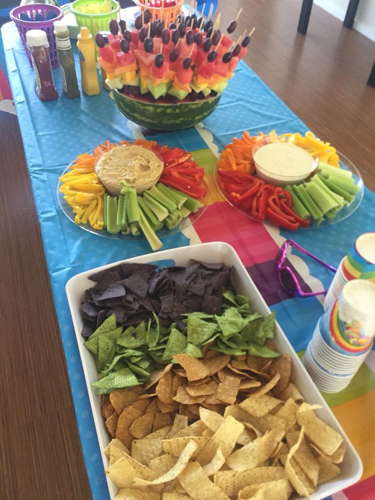 a table topped with bowls filled with chips and veggies next to dips