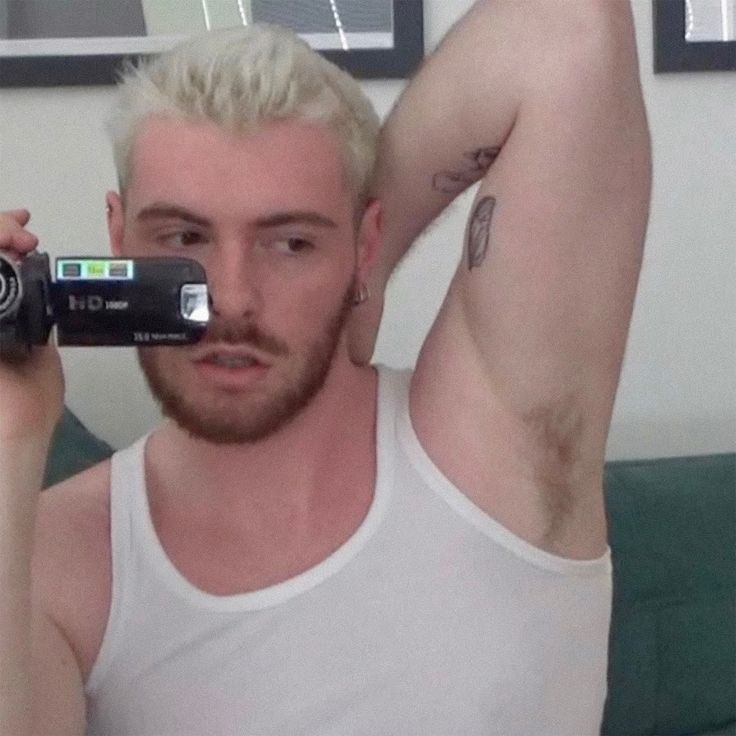 a man taking a selfie with his camera in front of him, wearing a white tank top