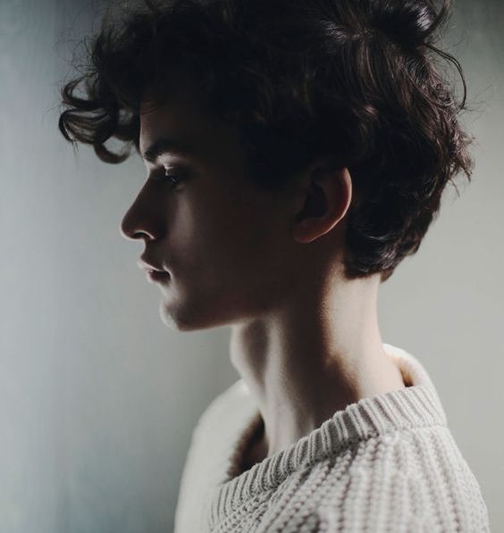 a woman with curly hair standing in front of a wall and looking off to the side