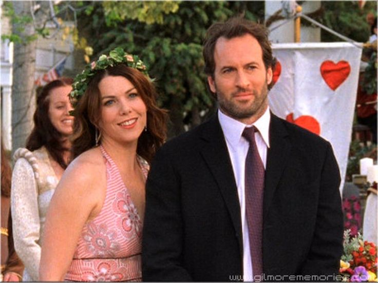 a man and woman standing next to each other in front of people wearing flower crowns