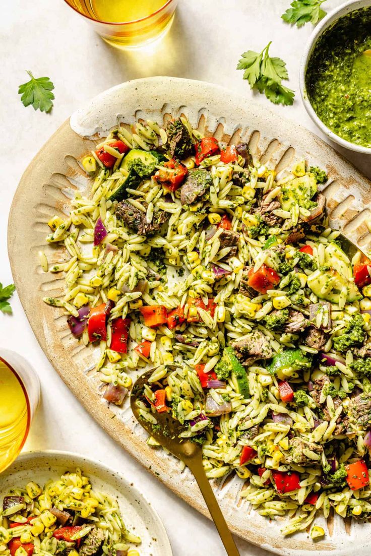 a platter filled with pasta salad next to two bowls of pesto sauce