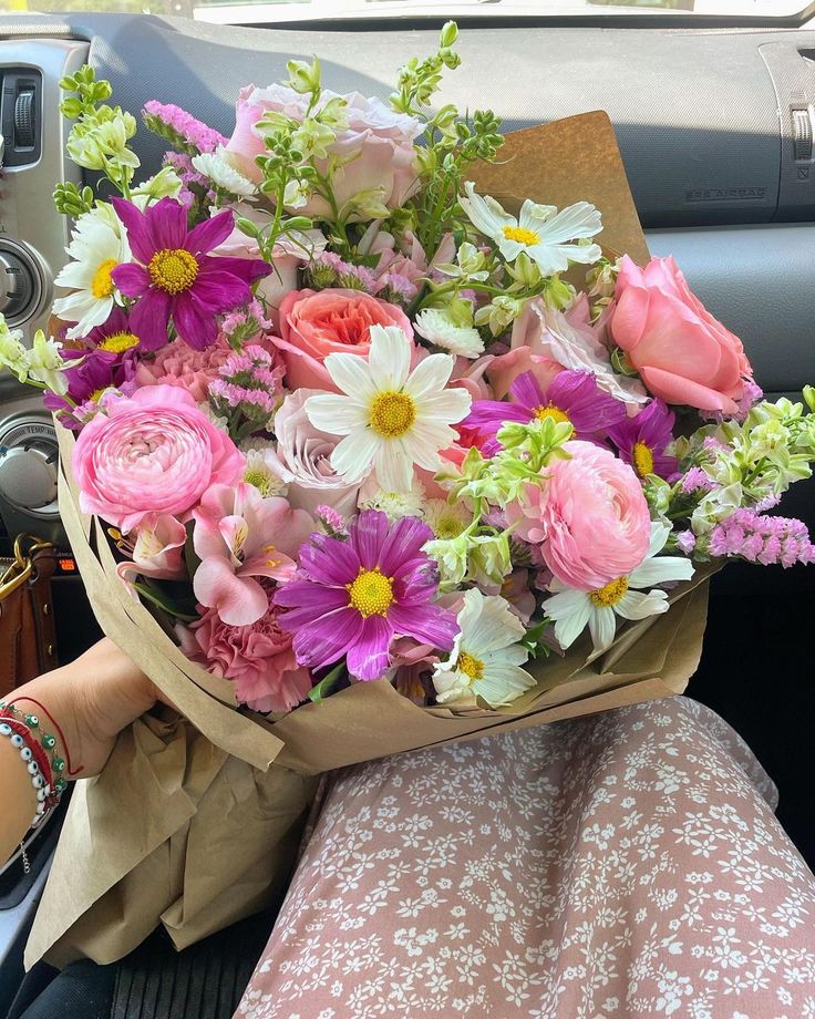 a bouquet of flowers sitting in the passenger seat of a car with someone holding it