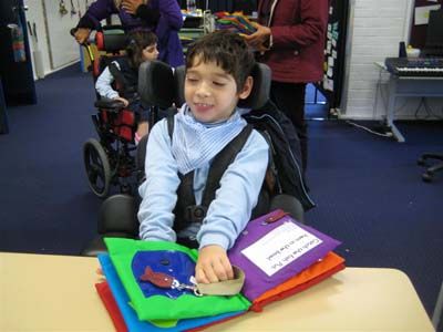 a young boy sitting in a wheel chair at a table with some books and scissors