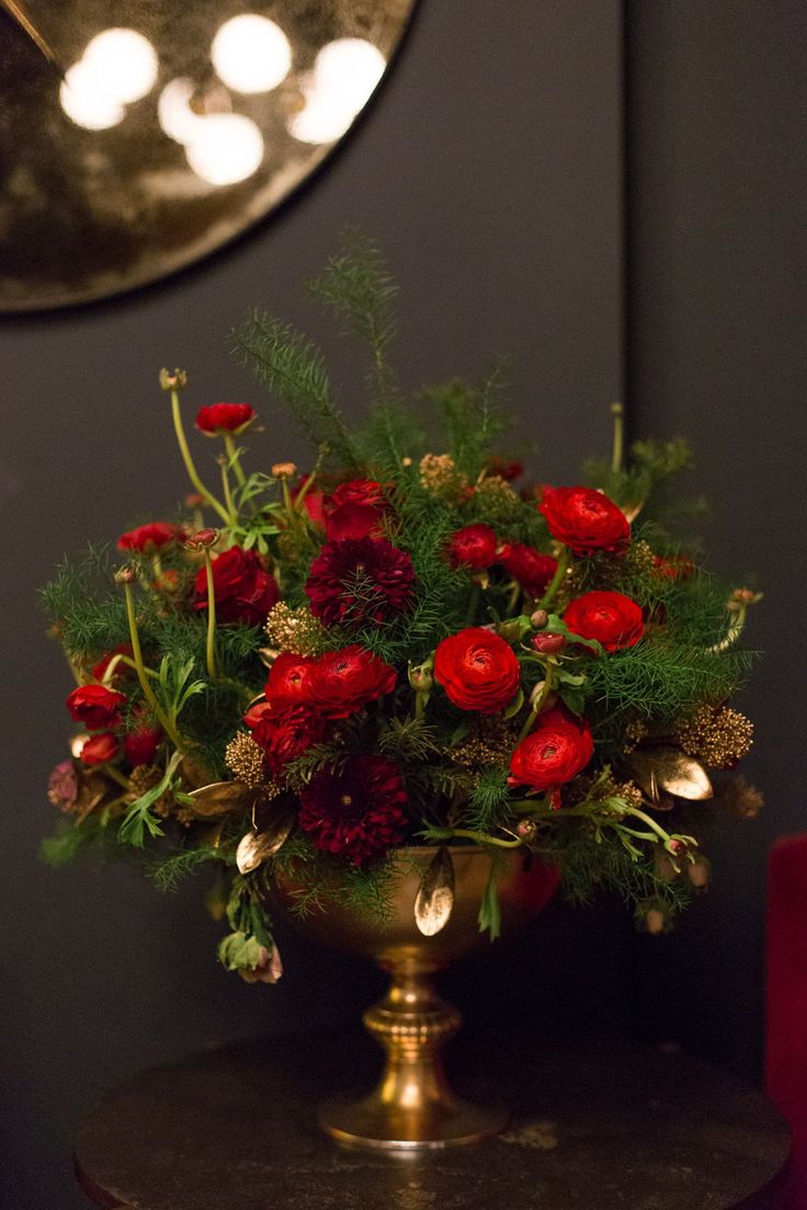 a gold vase filled with red flowers sitting on top of a table next to a mirror