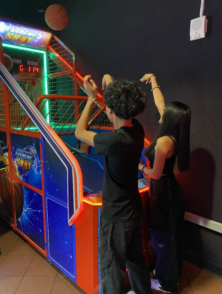 two people playing an arcade basketball game on the wall in front of a neon sign