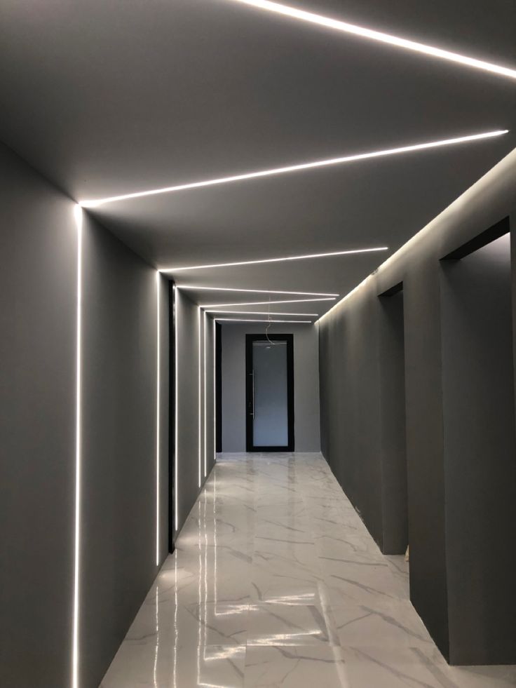 an empty hallway with white marble floors and lights on the ceiling is lit by recessed lighting