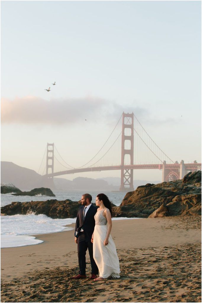 a bride and groom standing on the beach in front of the golden gate bridge