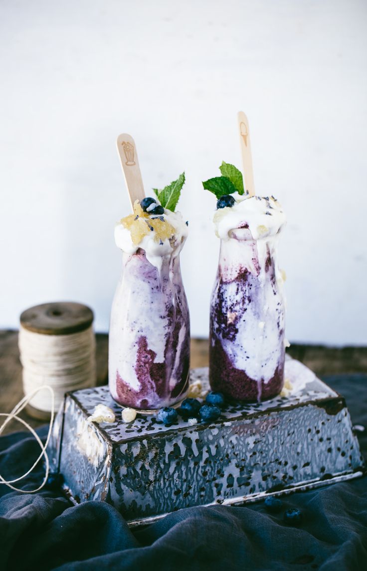 two ice cream sundaes with blueberries and whipped cream on top are sitting on a piece of wood