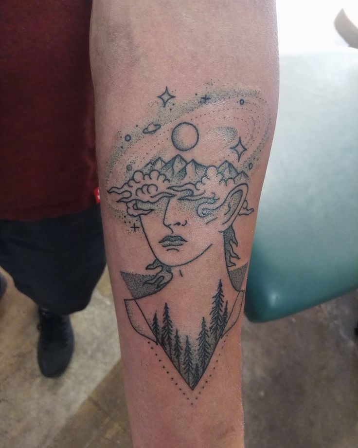 a woman's arm with a tattoo on it that has trees and mountains in the background