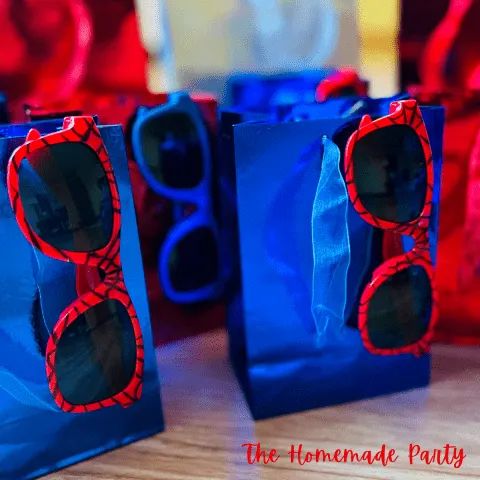 two blue bags with red sunglasses on them sitting on top of a wooden table in front of some glasses