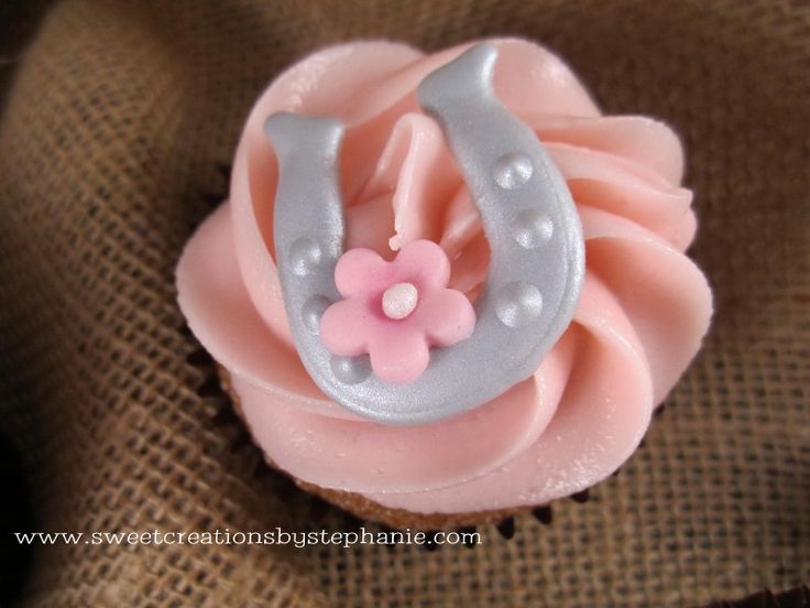 a cupcake decorated with pink frosting and a silver horseshoe on it's side